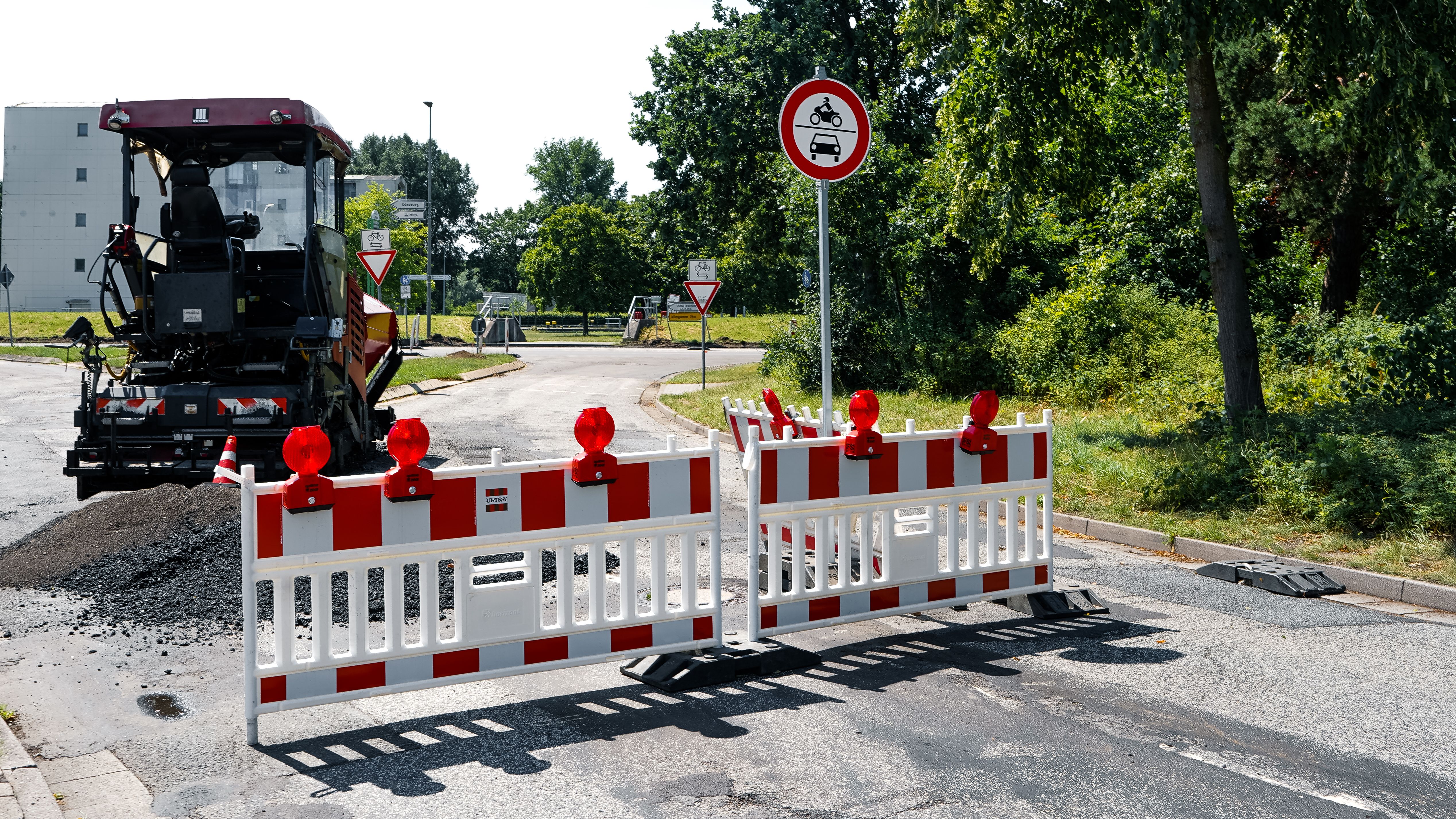 A roadwork scene in Geesthacht, Germany, showing barricades and construction machinery on a sunny day.
