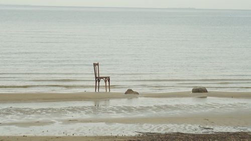 Free A lone chair on a tranquil beach with gentle waves, conveying solitude. Stock Photo