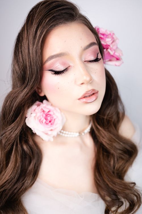 Free A close-up portrait of a young woman with pink floral accents, showcasing elegant makeup and hairstyle. Stock Photo