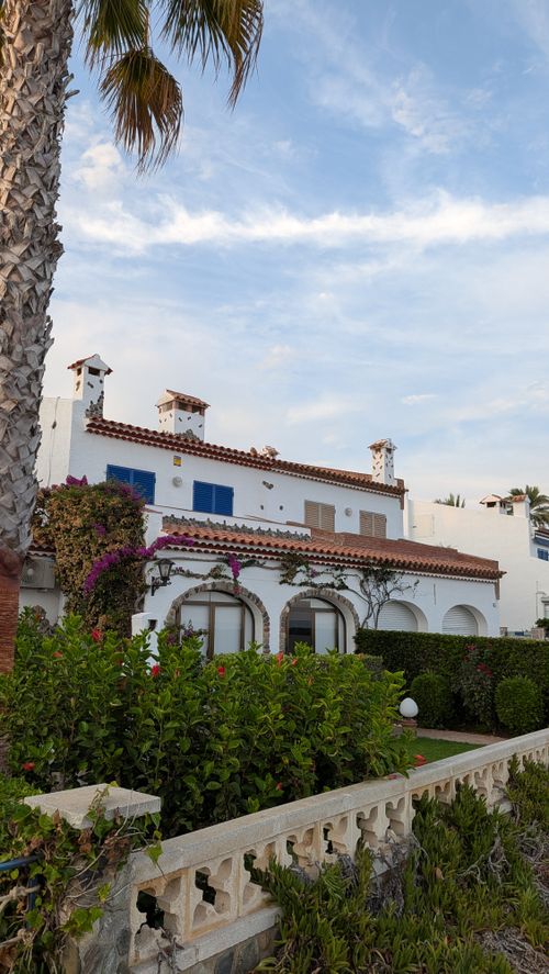 Free Charming Mediterranean villa with vibrant garden and classic white architecture under clear skies. Stock Photo