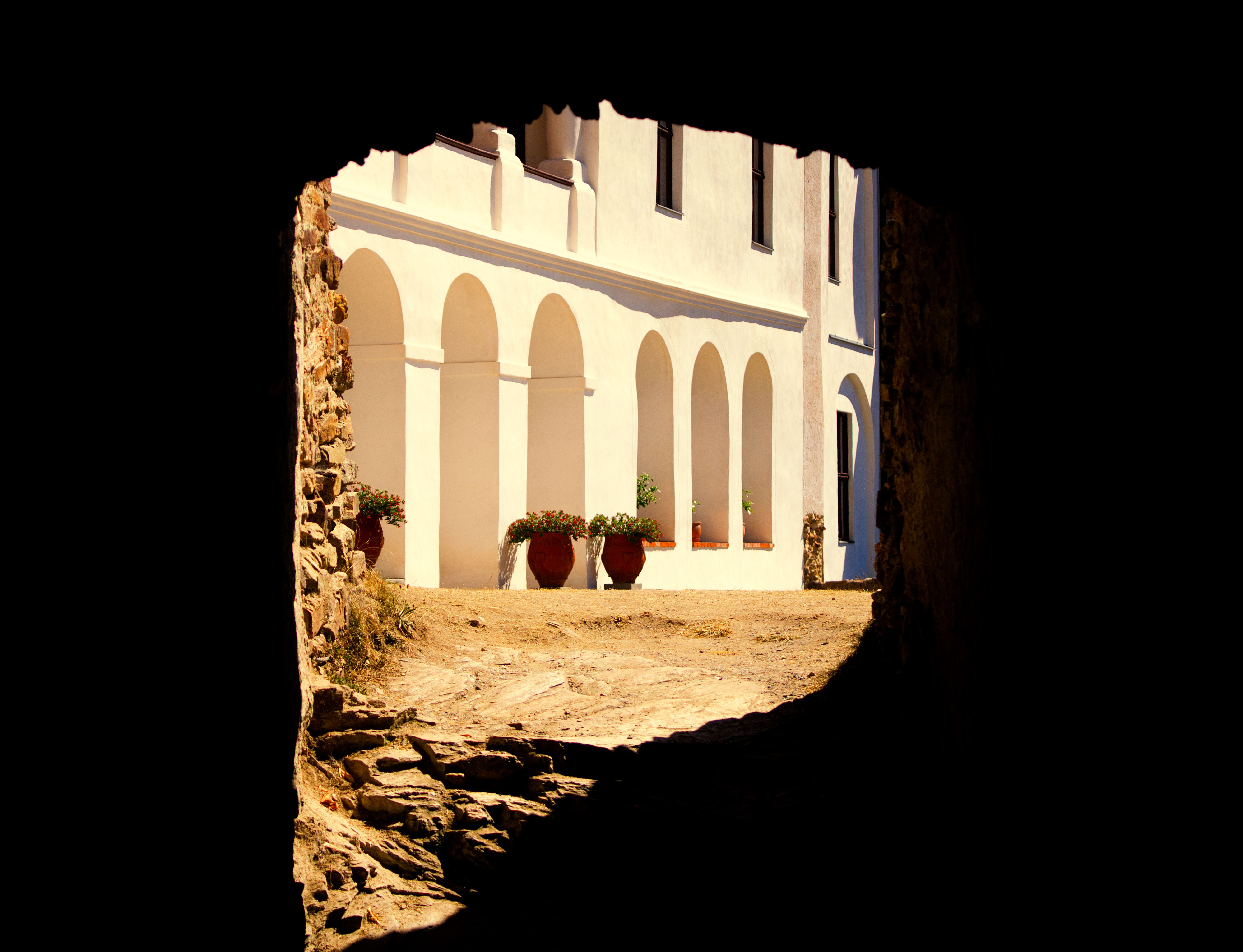 A view through a stone tunnel to a historic building with arches and bright facade, captured in warm lighting.