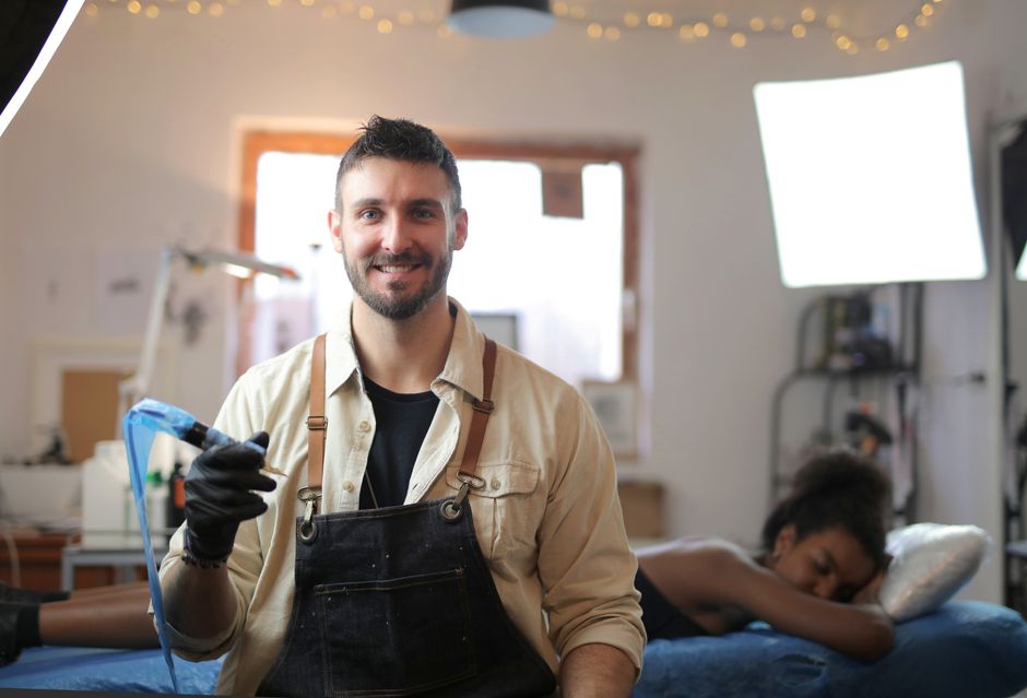 Mentor guiding an adult apprentice in a tattoo studio, highlighting professional maturity.