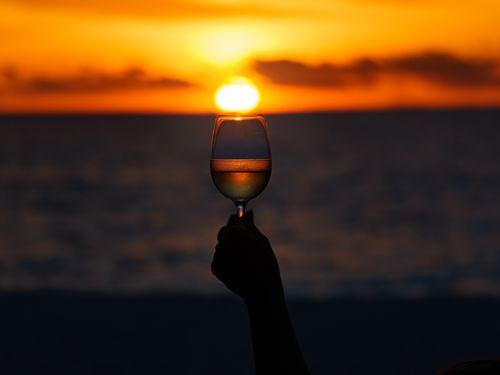 Free A silhouette of a hand holding a wine glass against a vibrant sunset in the Maldives. Stock Photo