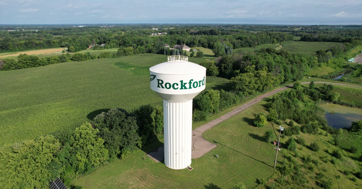 Aerial shot of the Rockford water tower surrounded by lush green fields and forests in summer.