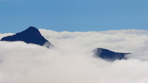 Free Peaceful mountain landscape with peaks emerging above a sea of clouds under a clear blue sky. Stock Photo