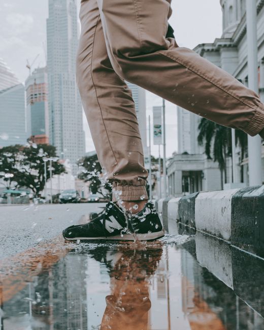A person walks stylishly through a city street, splashing water as they step in a puddle.