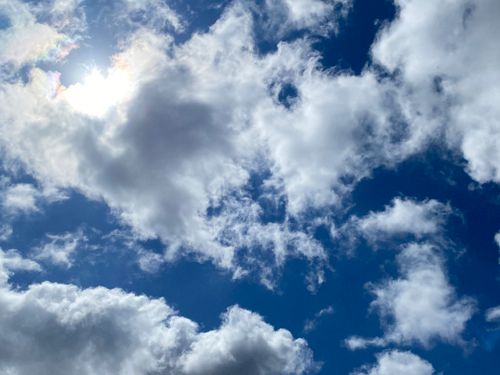 Free A serene view of fluffy clouds in a bright blue sky with sunlight peeking through. Stock Photo