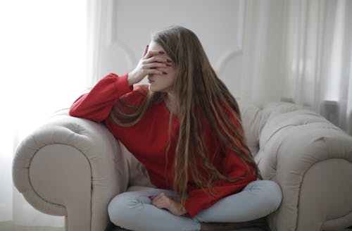 Free Woman in Red Long Sleeve Shirt Sitting on White Armchair Stock Photo