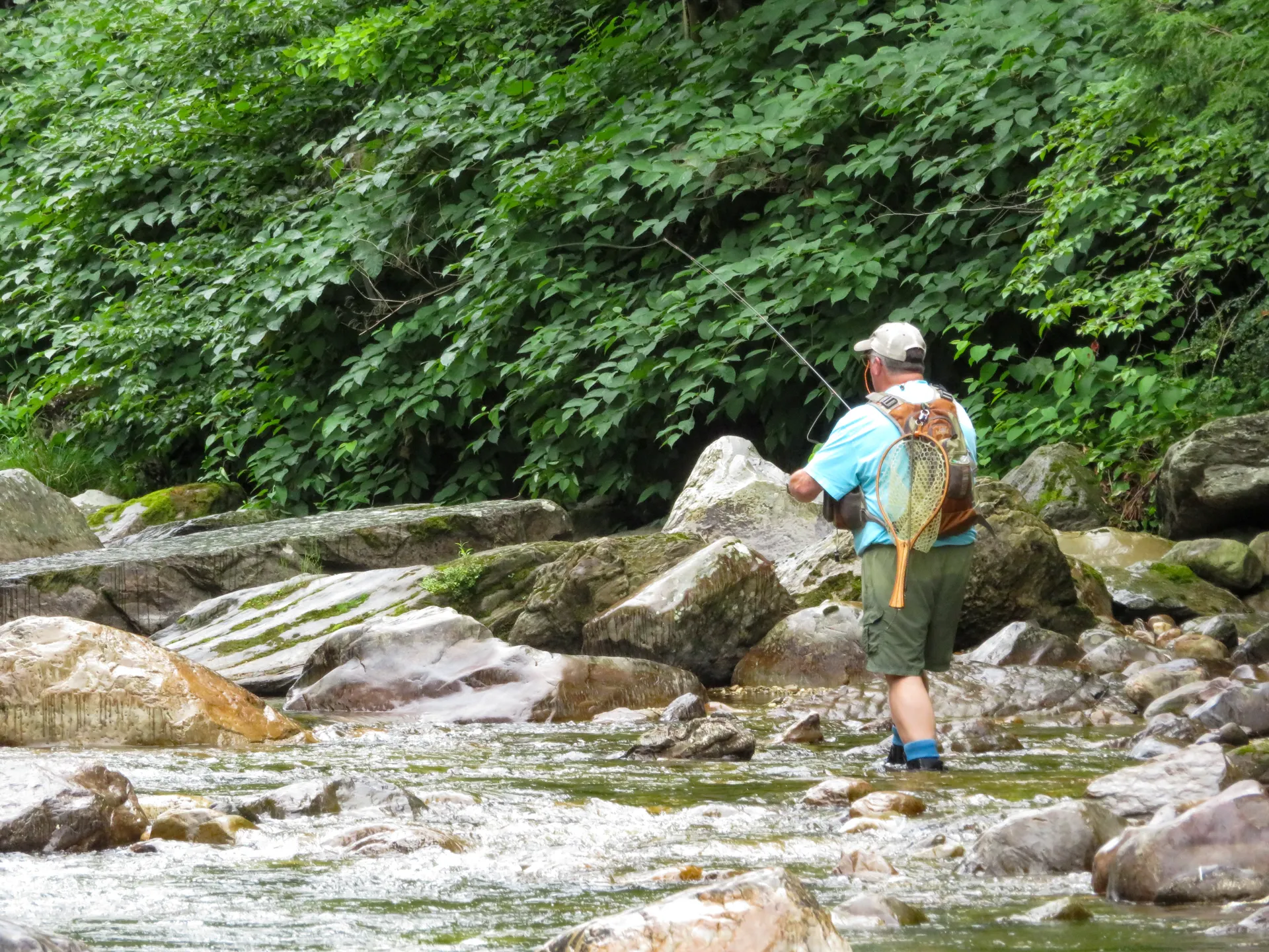 A man fly fishing in a quiet Vermont river surrounded by green trees and rocks. A man fly fishing in a quiet Vermont river surrounded by green trees and rocks.
