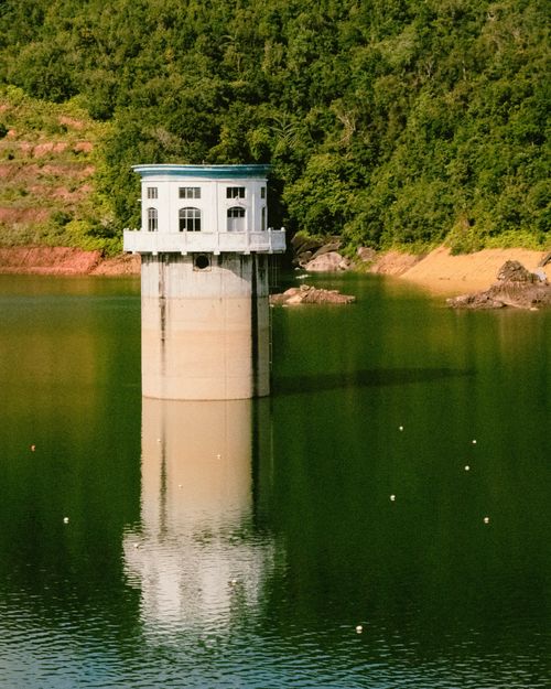 Free A tower reflecting in a serene reservoir surrounded by lush greenery in Penang, Malaysia. Stock Photo
