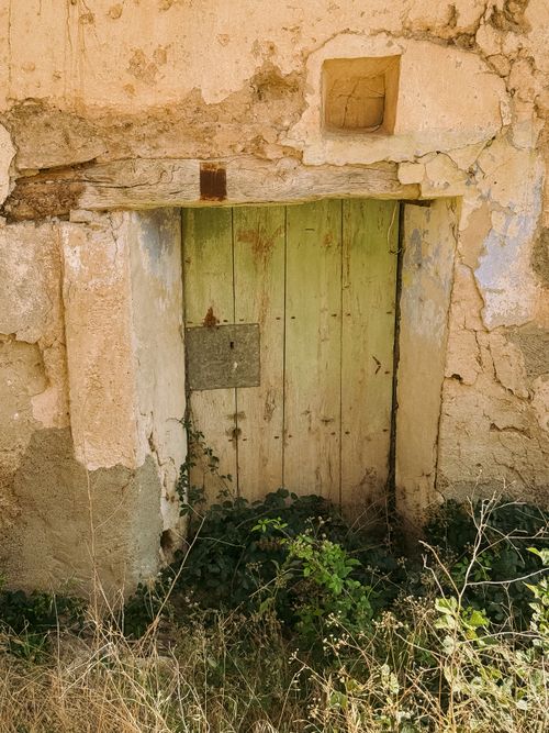 Free A rustic, abandoned doorway surrounded by overgrown plants in Pórtalrubio, Aragón. Stock Photo