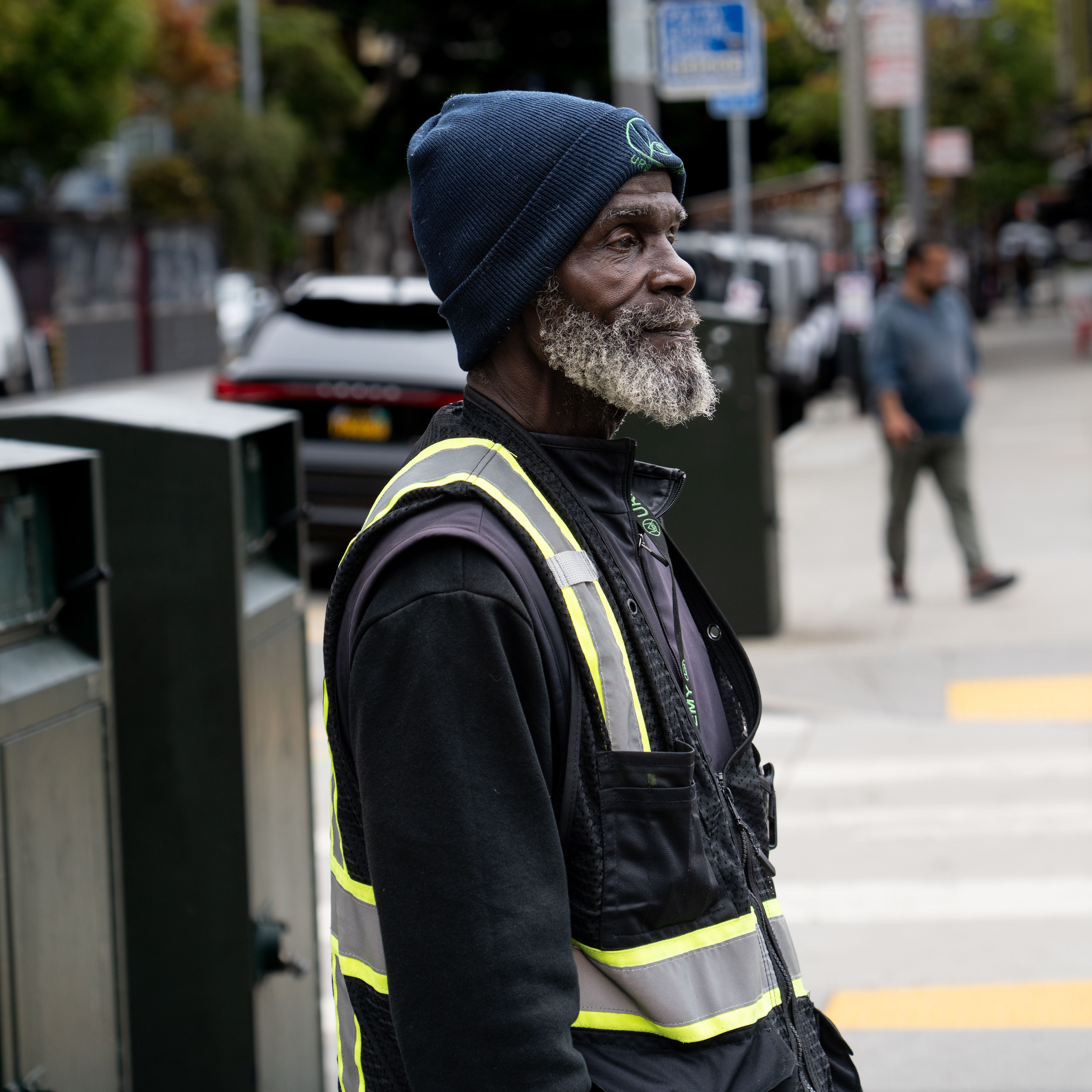 Street worker in San Francisco wearing a beanie and safety vest, captured on a city sidewalk.