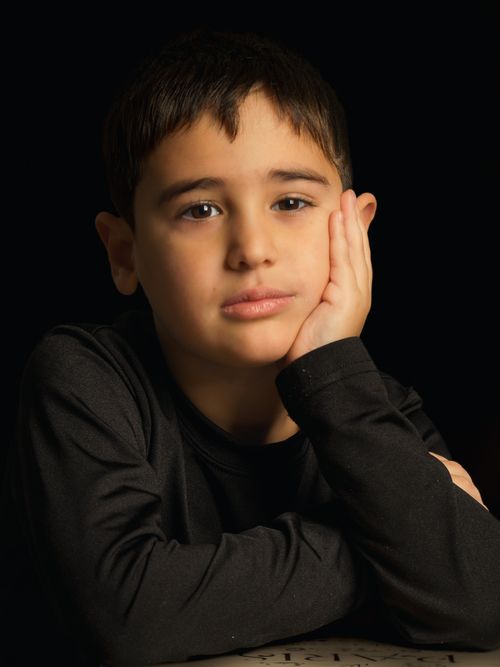 Free Portrait of a thoughtful child resting chin on hand against a dark background. Stock Photo