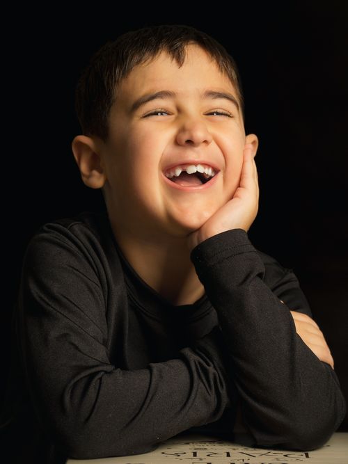 Free A young boy in a studio setting joyfully laughing, with a dark background creating a dramatic effect. Stock Photo