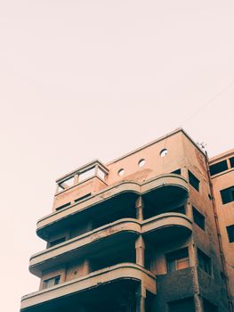 Urban apartment building with vintage architecture and pastel tones against a clear sky.