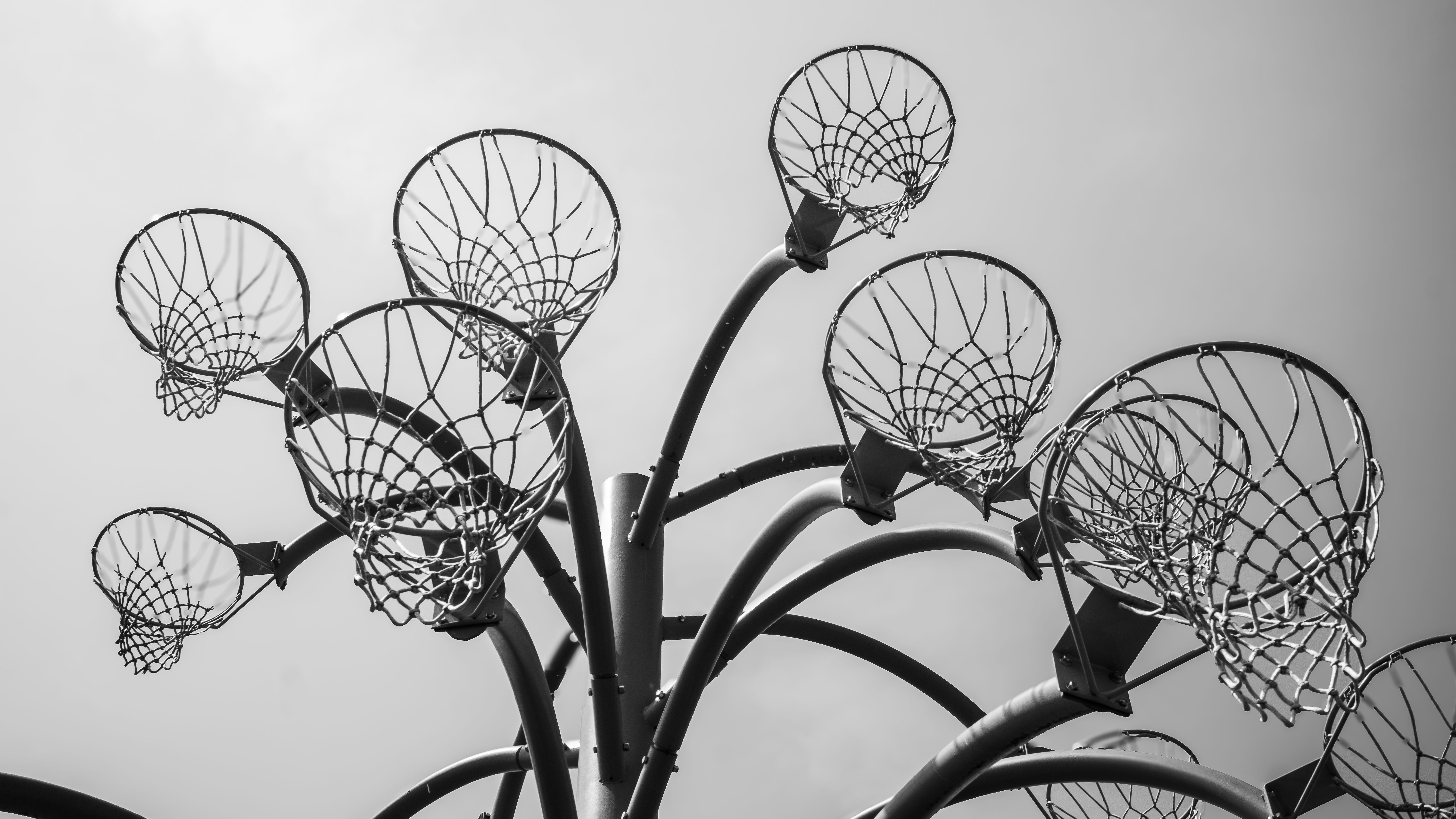 A unique black and white photo of a sculptural arrangement of basketball hoops viewed from below.