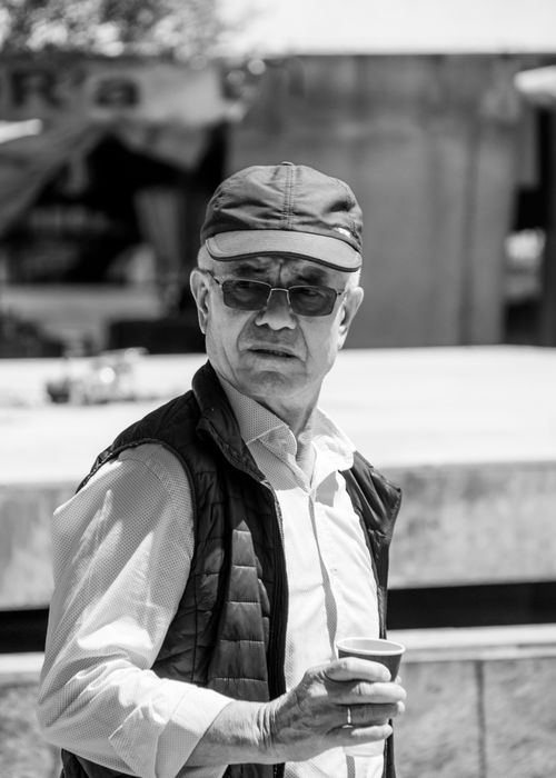 Free Black and white portrait of a senior man holding a coffee cup, wearing sunglasses and a cap. Stock Photo