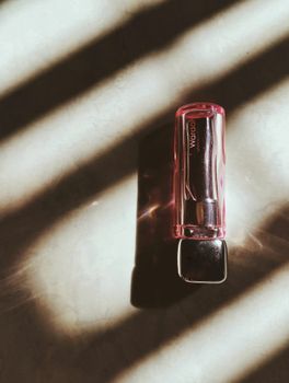 A lipstick tube casting shadows in dramatic striped light, emphasizing beauty and elegance.