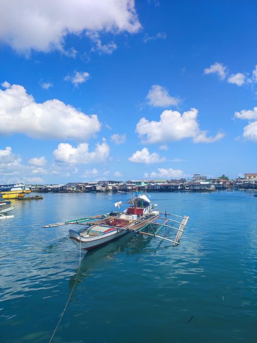 Free A traditional boat floats on tranquil blue waters of Bongao, Philippines, beneath a vibrant blue sky and scattered clouds. Stock Photo