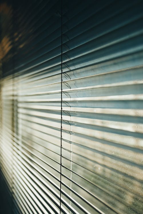 Modern metal Venetian blinds in white color covering window and sunlight coming through