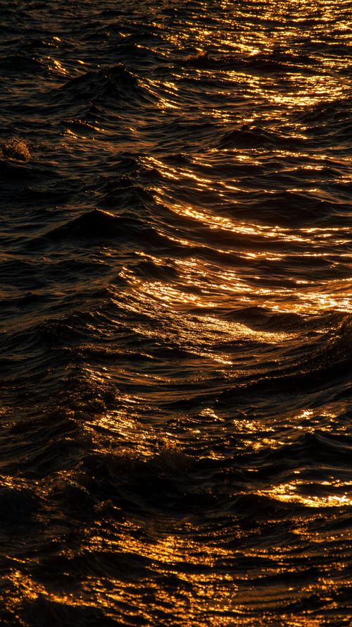 Free Golden light reflects off evening waves creating a serene and dramatic sea view. Stock Photo
