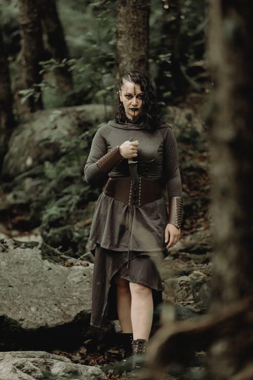Free A woman in gothic attire poses in a shadowy forest, evoking a sense of mystery. Stock Photo