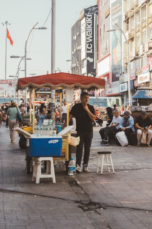 Free Busy street scene with street vendor cart and pedestrians, capturing the lively urban atmosphere. Stock Photo