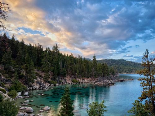 Free Peaceful Lake Tahoe shoreline with vibrant sunset sky and scenic forested landscape. Stock Photo