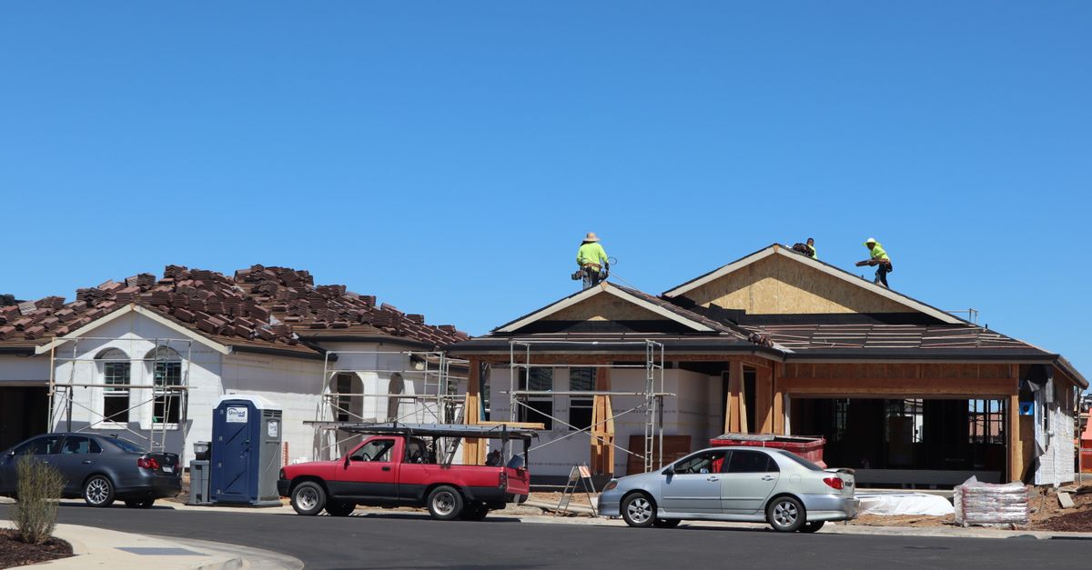 Construction workers on roof of newly built suburban home under clear blue sky.