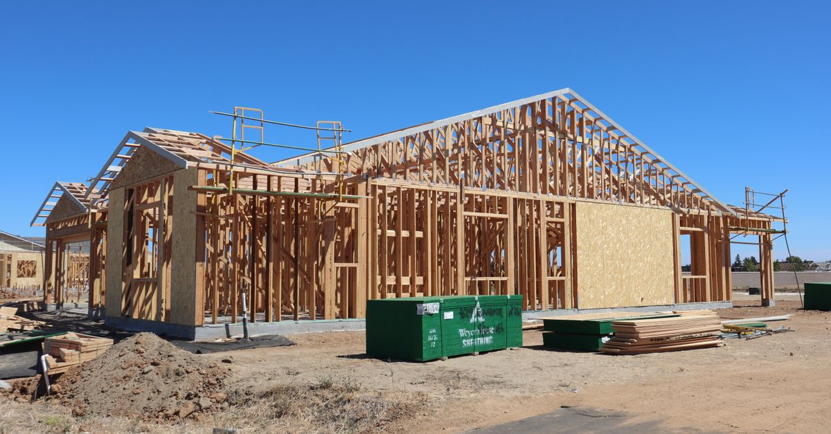 Wooden house frame construction under clear blue sky, sunny day.
