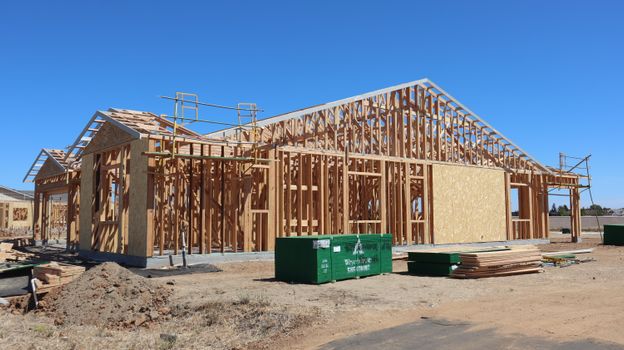 Wooden house frame construction under clear blue sky, sunny day.