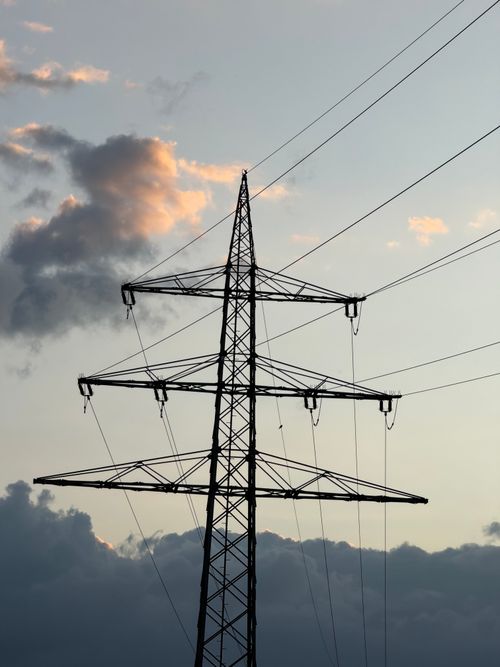Free A striking view of a silhouetted power line tower against a dramatic sunset sky with clouds. Stock Photo