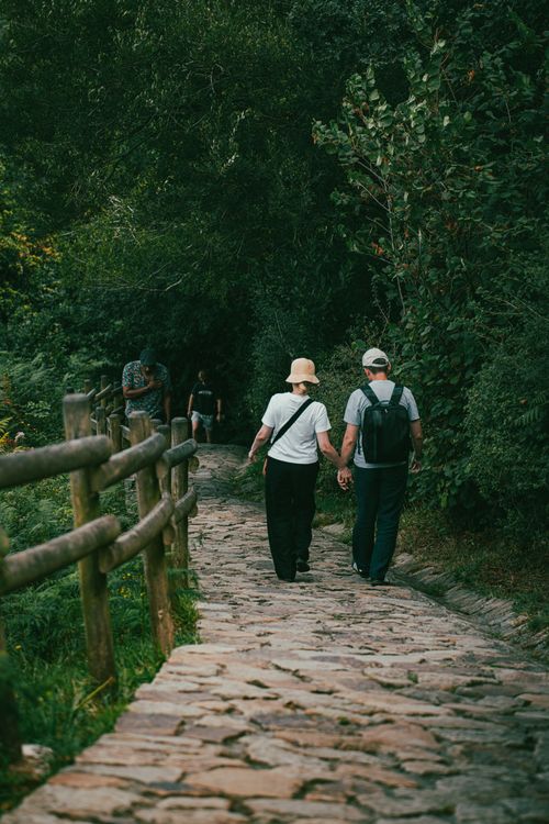 Free A couple walking hand in hand on a scenic forest path at Gaztelugatxeko Doniene, Spain. Stock Photo