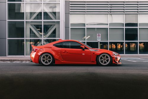 Free Stylish red sports car parked in front of a modern building, emphasizing design and urban automotive lifestyle. Stock Photo