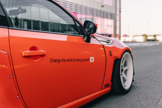 Vibrant orange sports car with an inspirational message on the side, parked outdoors.
