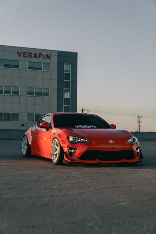 Free Vibrant red sports car parked in an urban environment with modern building backdrop. Stock Photo