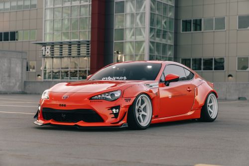 Free Dynamic photo of a vivid red sports car with custom modifications parked in a modern urban setting. Stock Photo