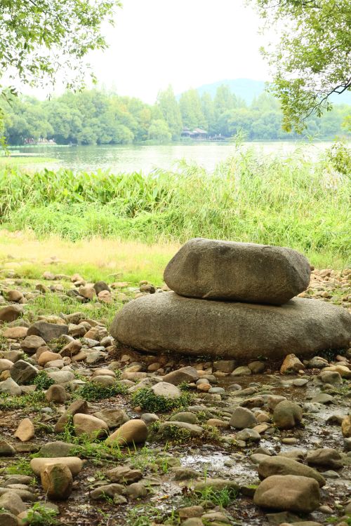Free Idyllic riverbank scene featuring stacked stones, lush greenery, and calm water. Stock Photo