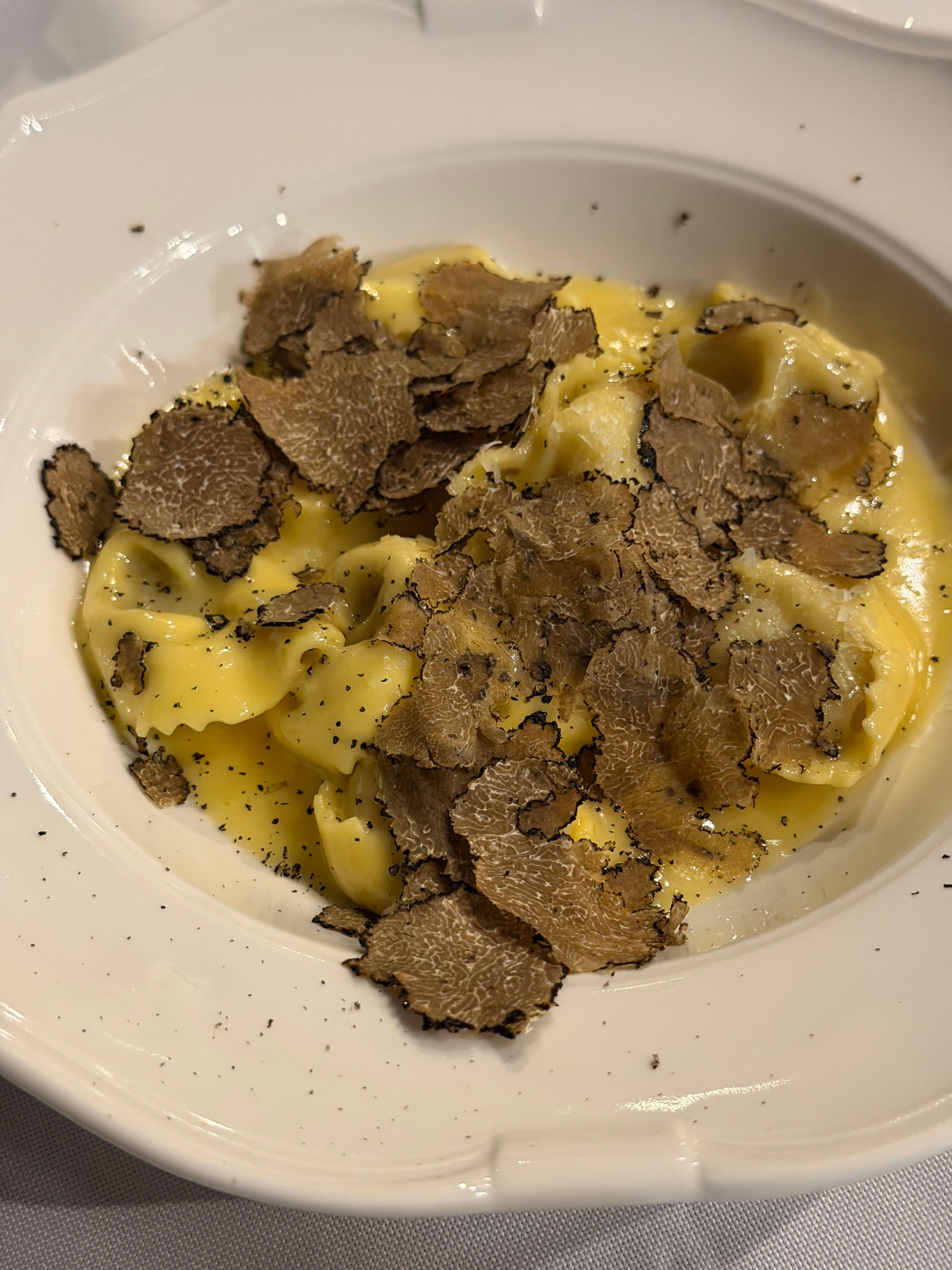 A small ramekin of pale ivory truffle butter studded with tiny black truffle flecks, next to a whole black truffle and a butter knife