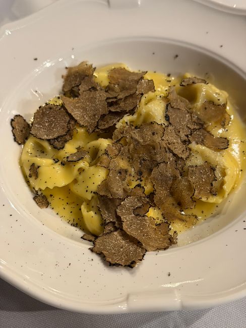 A small ramekin of pale ivory truffle butter studded with tiny black truffle flecks, next to a whole black truffle and a butter knife