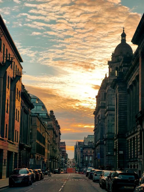 Free A vibrant street scene in Glasgow at sunset, highlighting historical architecture under a dramatic sky. Stock Photo
