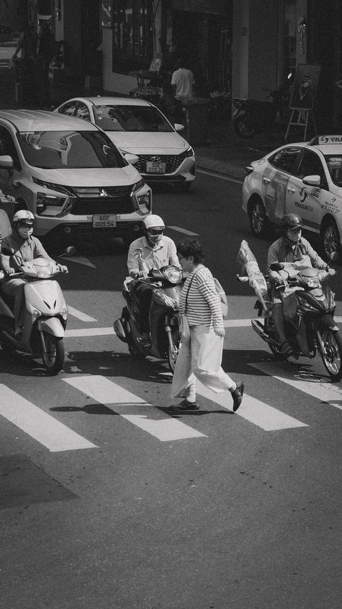 Free Black and white scene of pedestrians crossing a busy street in Vietnam, illustrating urban life. Stock Photo