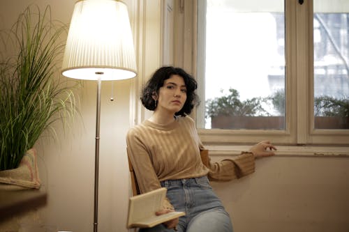 Free Woman in Brown Crew Neck Shirt and Blue Denim Jeans Sitting on Chair Stock Photo