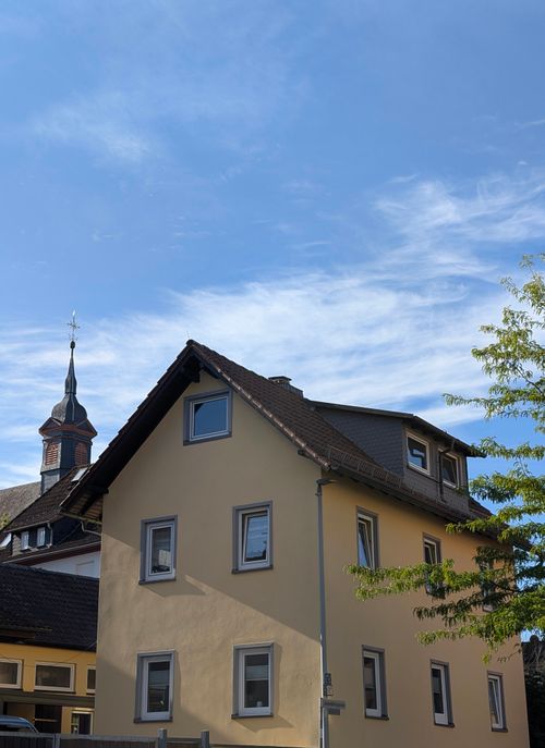 Free A quaint residential house with a church steeple in the background under a clear blue sky. Stock Photo