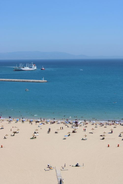 Free A vibrant beach scene with people relaxing and a ship passing in Tangier, Morocco. Stock Photo
