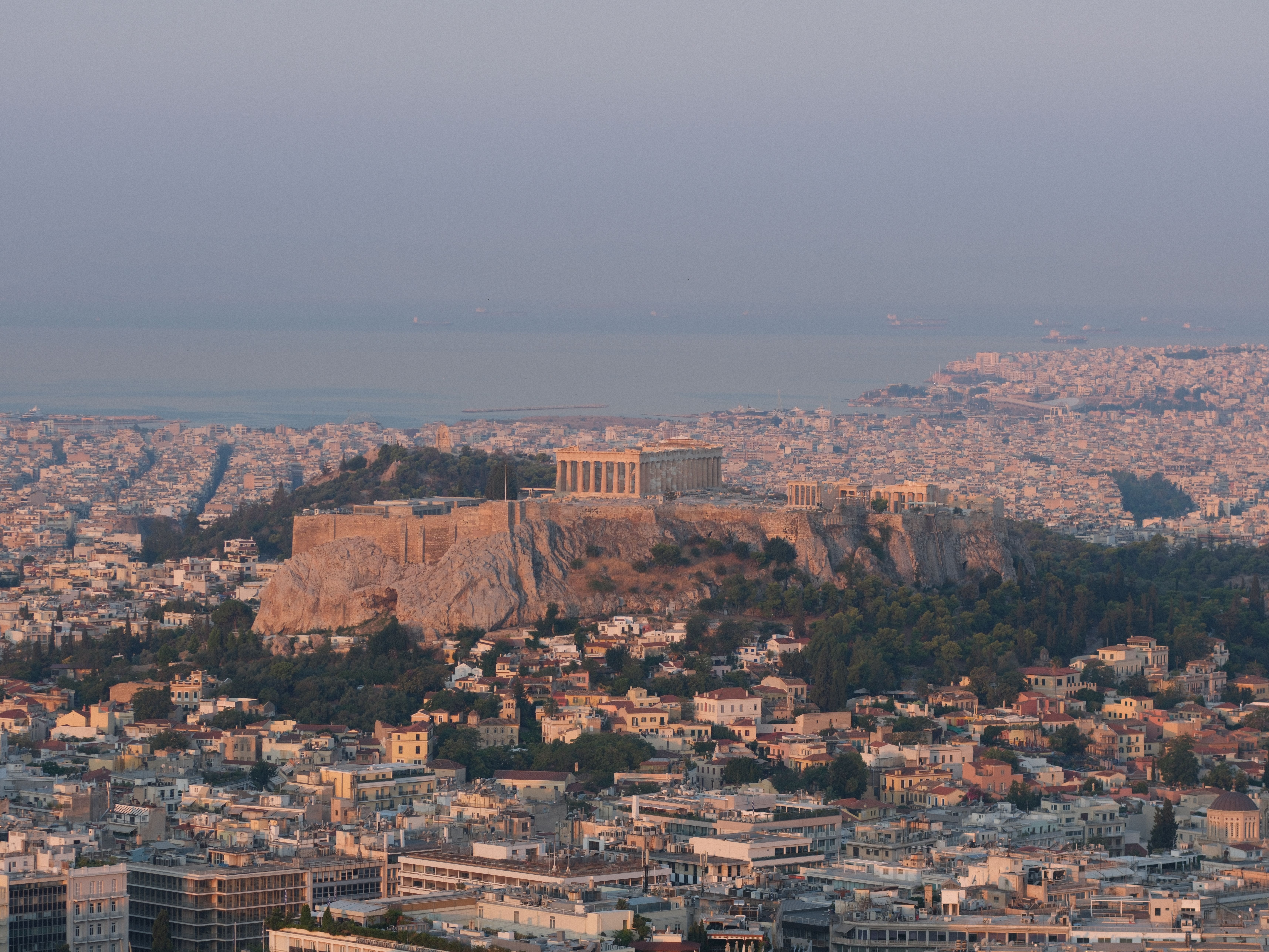Vue aérienne de l'Acropole d'Athènes au coucher du soleil, surplombant la ville s'étendant jusqu'à la mer à l'horizon.