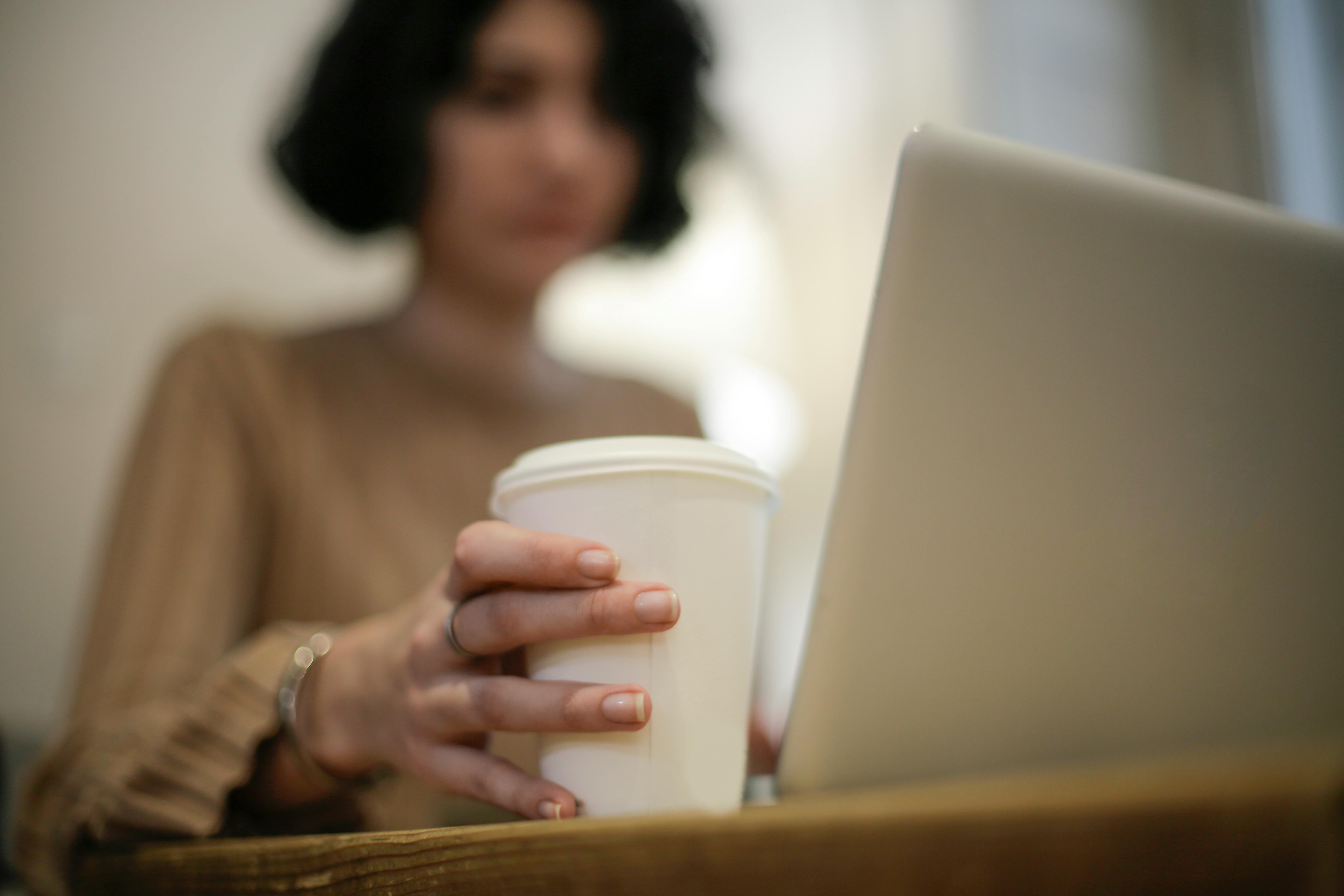 A woman with a coffee cup working on a laptop, depicting a typical modern workday scenario.