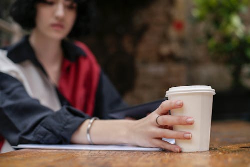 Woman in Red and Black Long Sleeve Holding White Disposable Cup