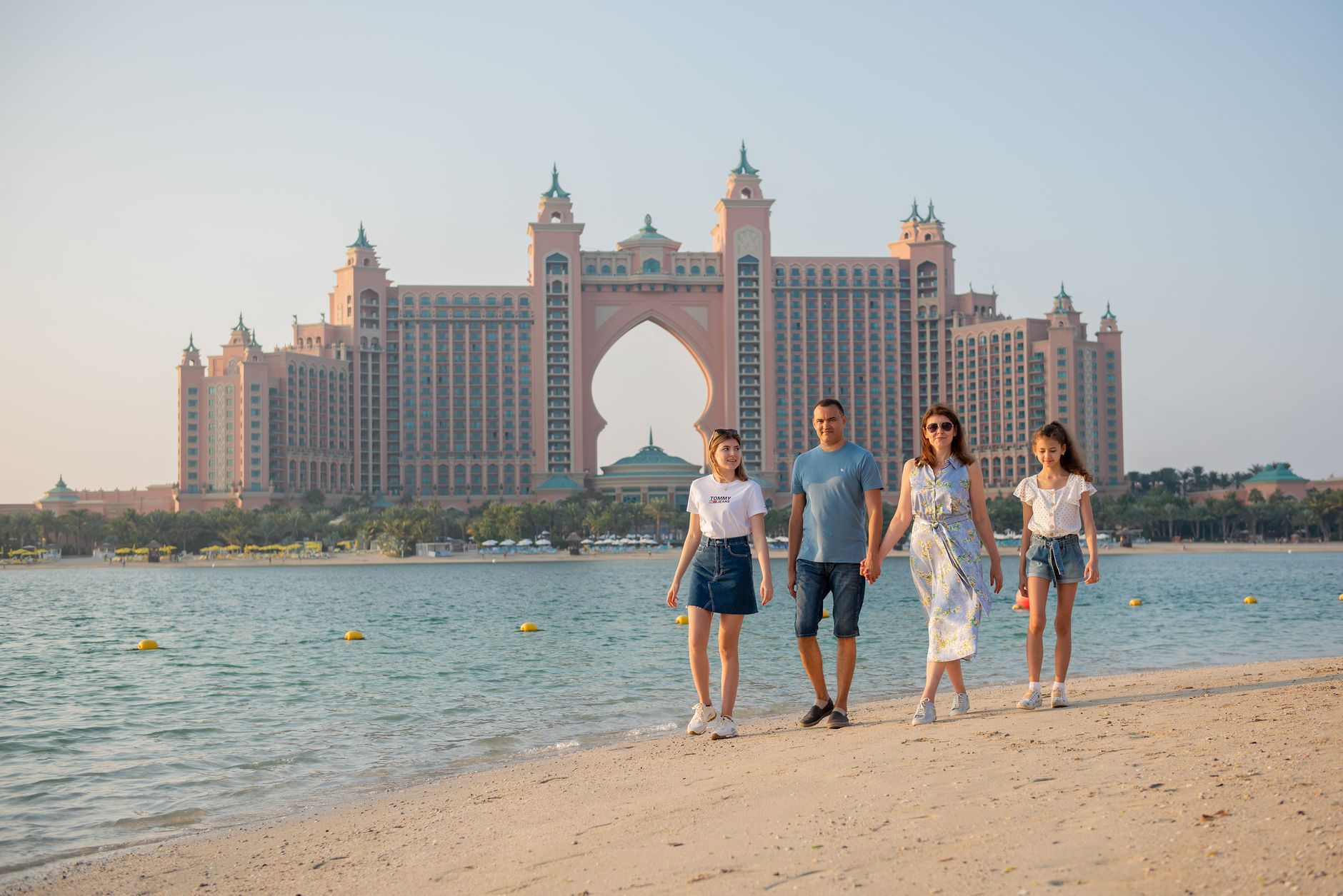 Family walking along the beach with Atlantis The Palm Hotel in the background, Dubai.