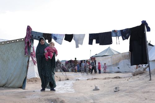 Free A woman holding a child in a refugee camp, clothing hung out to dry. Stock Photo